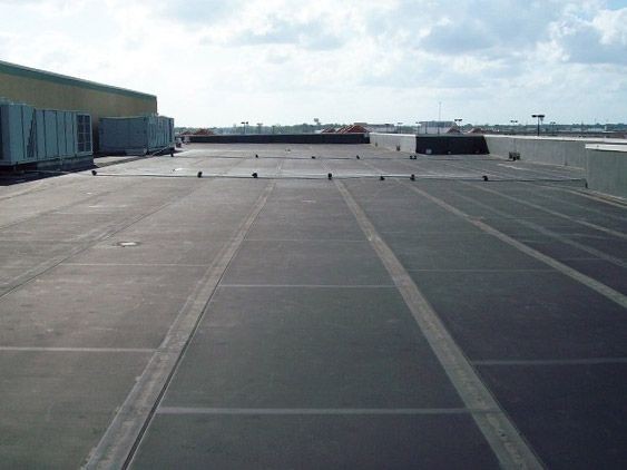 View of a flat commercial rooftop with black rubber roofing material and HVAC units in the background.