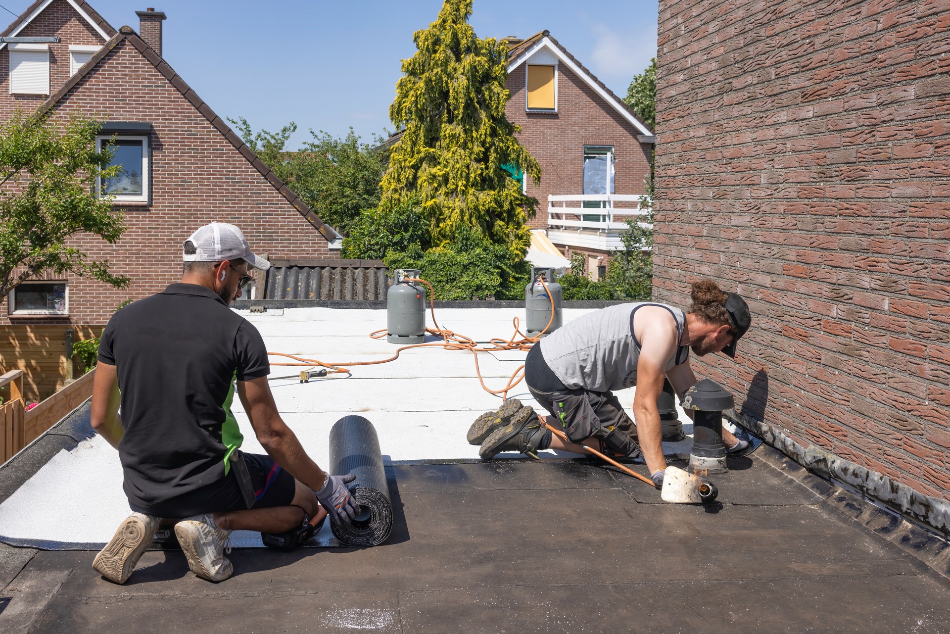 Workers flat roof preparing rolls of roofing felt or bitumen